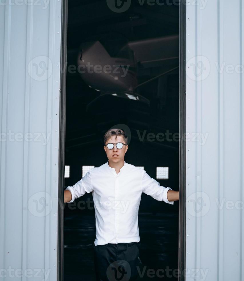 Ein gutaussehender Typ mit Sonnenbrille öffnet die Tür zum Hangar. foto