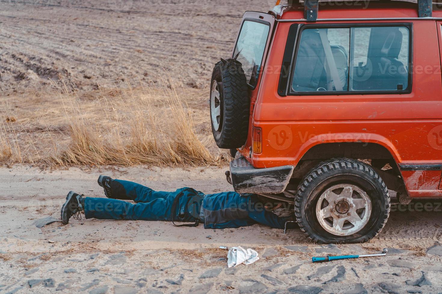Mann liegt unter einem 4x4-Auto auf einer unbefestigten Straße foto