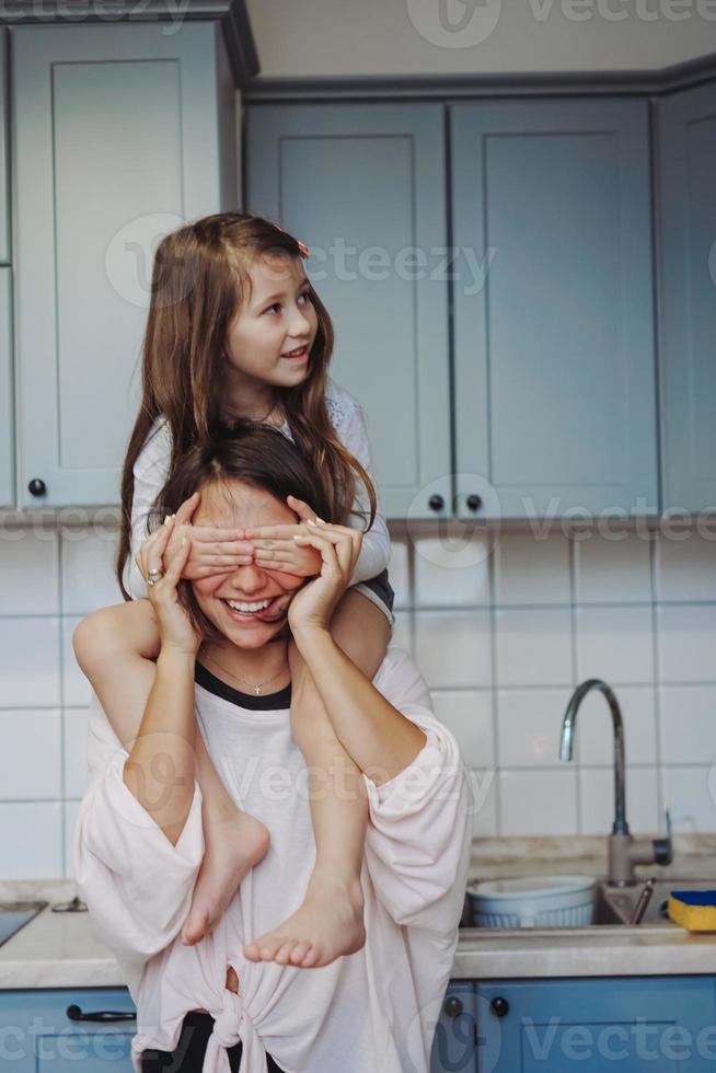 schöne kleine tochter, die ihre glückliche mutter huckepack trägt foto