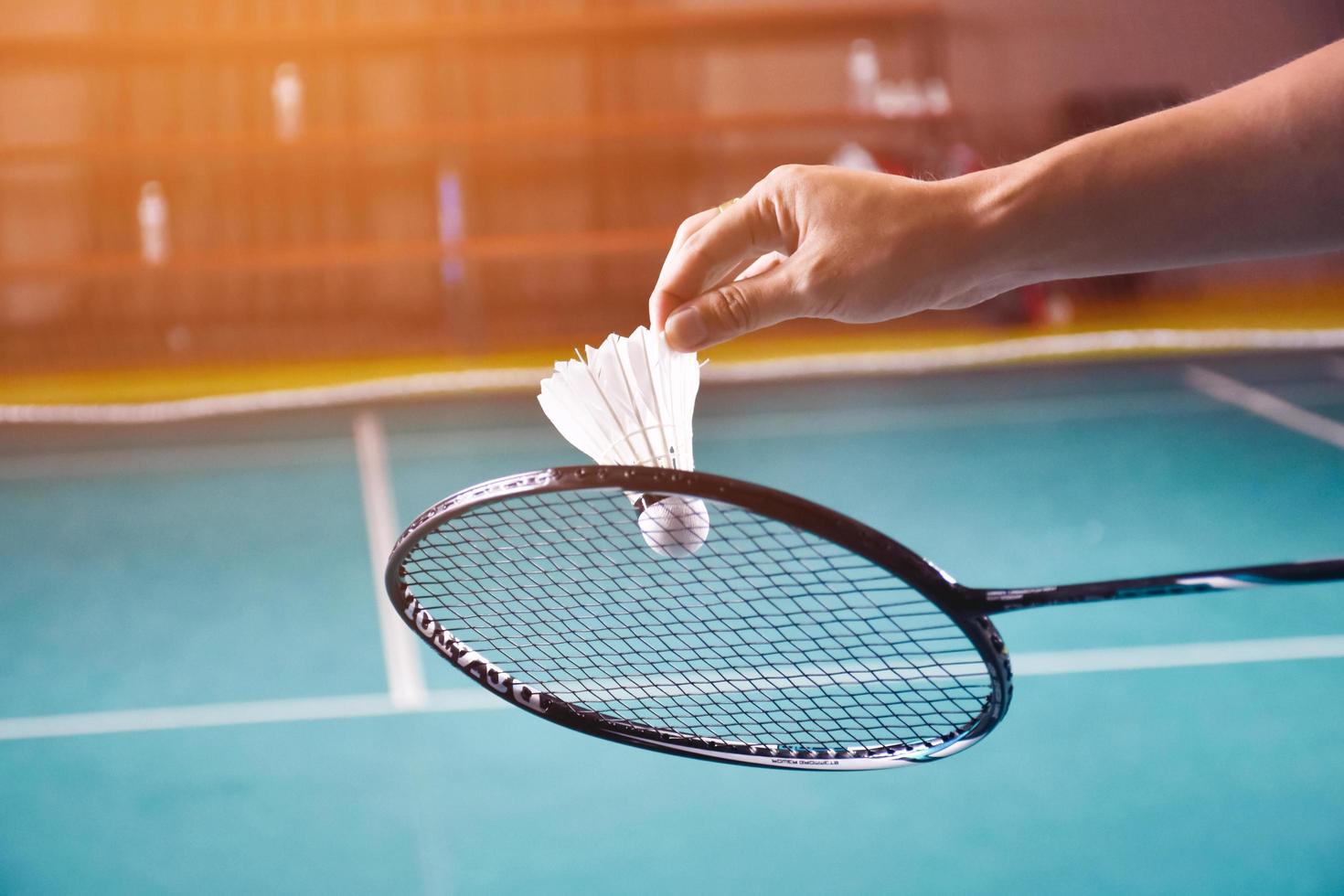 Badmintonschläger und alter weißer Federball, der den Spieler in den Händen hält, während er ihn über das Netz vor ihm serviert, verwischen den Hintergrund des Badmintonplatzes und selektiven Fokus foto