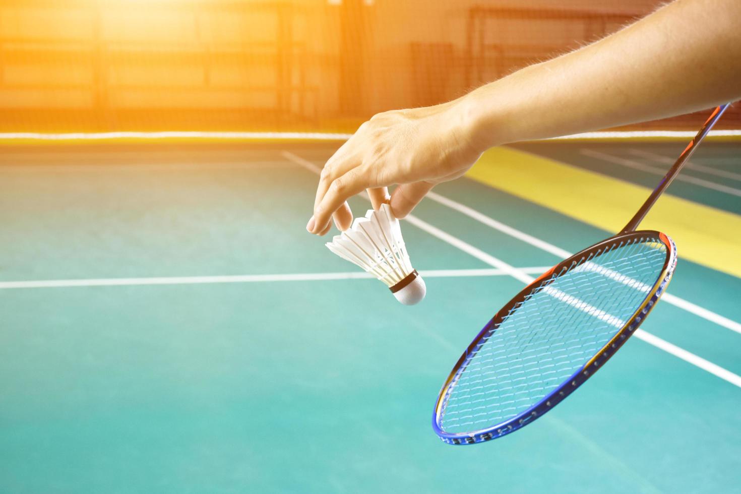 Badmintonschläger und alter weißer Federball, der den Spieler in den Händen hält, während er ihn über das Netz vor ihm serviert, verwischen den Hintergrund des Badmintonplatzes und selektiven Fokus foto