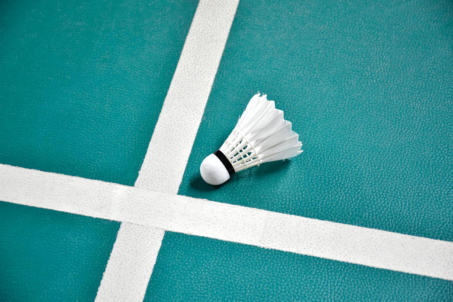 Cremeweißer Badmintonfederball auf grünem Boden im Indoor-Badmintonplatz, verschwommener Badmintonhintergrund, Kopierraum foto