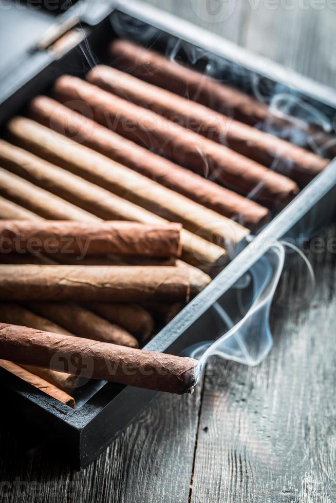 Rauch steigt von einer brennenden Zigarre auf hölzernen Humidor auf foto
