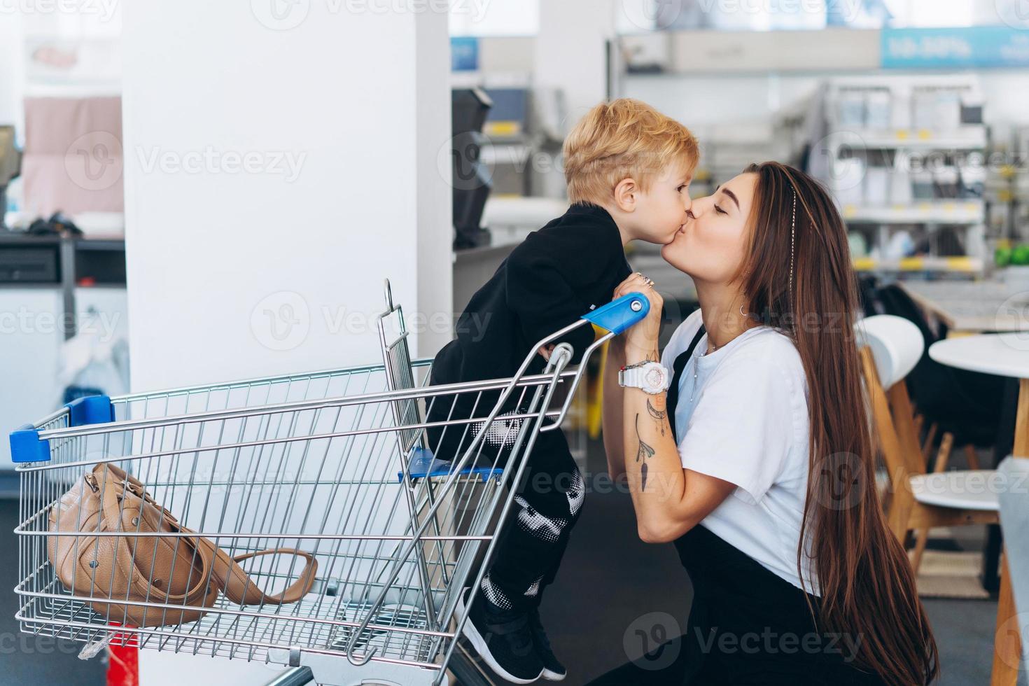 schöne mutter trägt ihren kleinen sohn im einkaufswagen foto