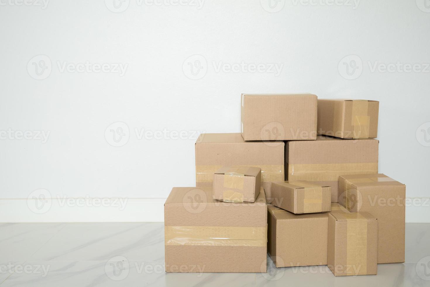Stapel Kartons für den Umzug, leerer Raum mit weißer Wand und Kartons mit Barcode ohne Marke auf dem Boden. Lieferung von Waren, Einkaufen. pappkartons auf grauem wandhintergrund. foto