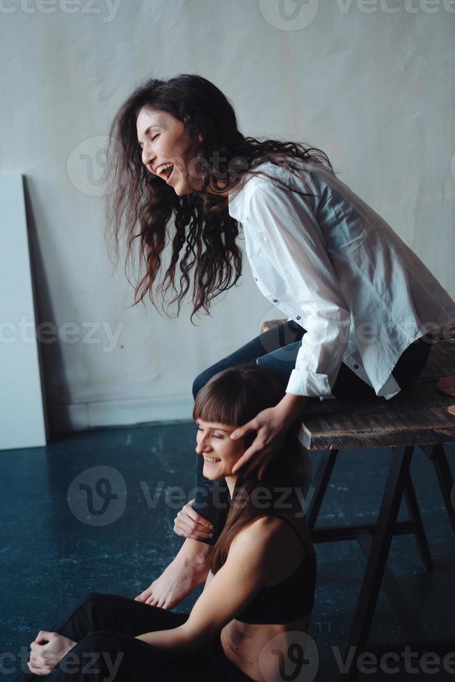Zwei Mädchen posieren für die Kamera, eines sitzt auf einem Stuhl, das andere auf dem Boden foto