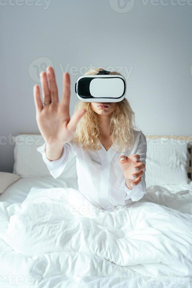 Mädchen sitzt auf einem Bett mit VR-Headset foto