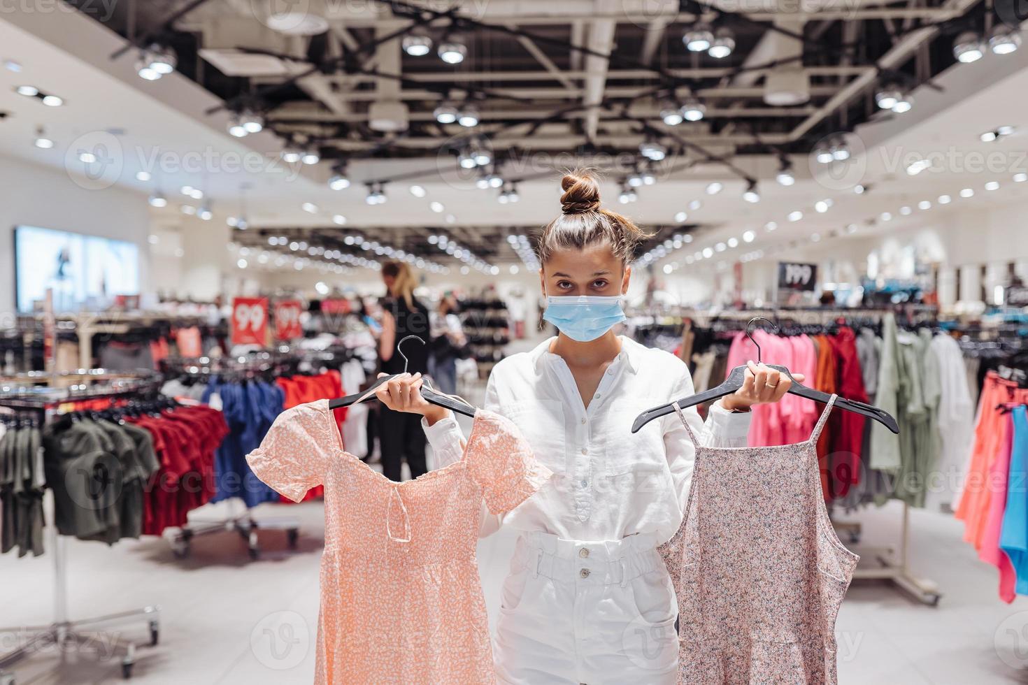 junge frau, die kleidung in einer bekleidungsboutique mit schützender gesichtsmaske einkauft foto