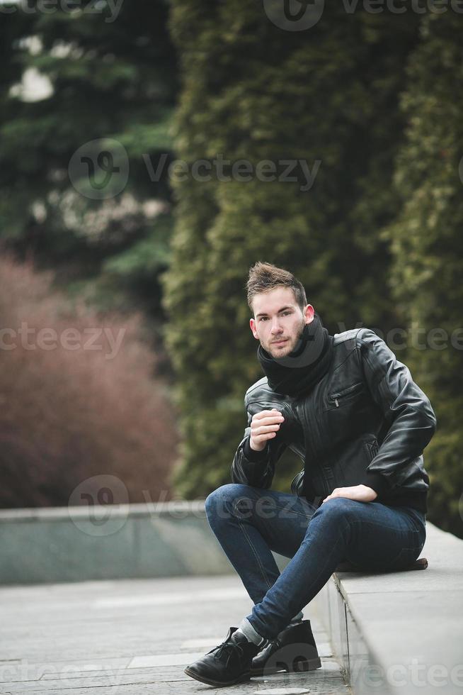 ein mann in jeans und schwarzer jacke sitzt auf einer platte foto