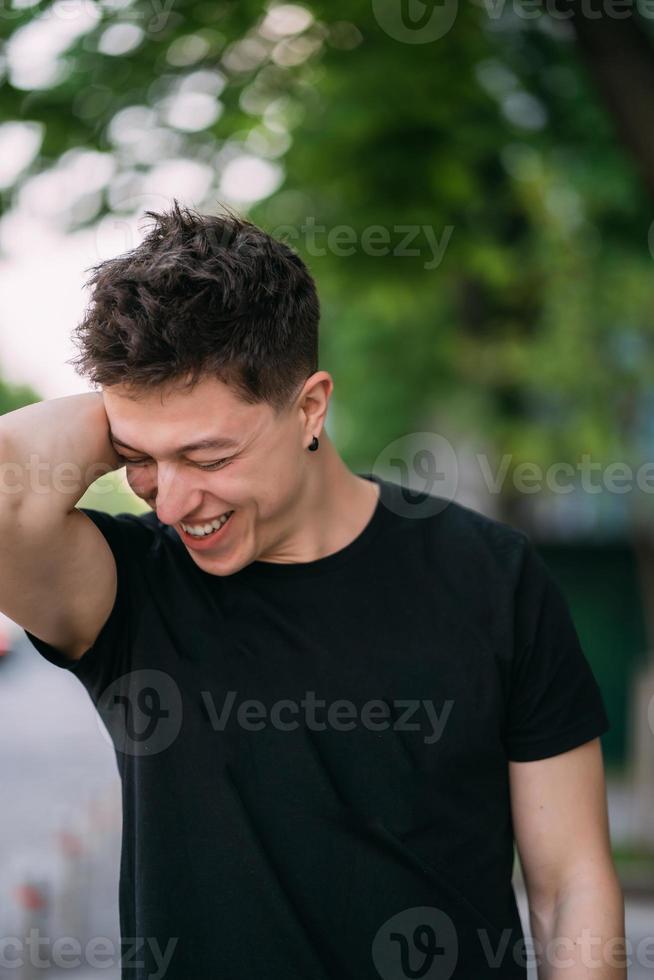 junger erwachsener mann in einem schwarzen t-shirt und jeans geht auf einer stadtstraße foto