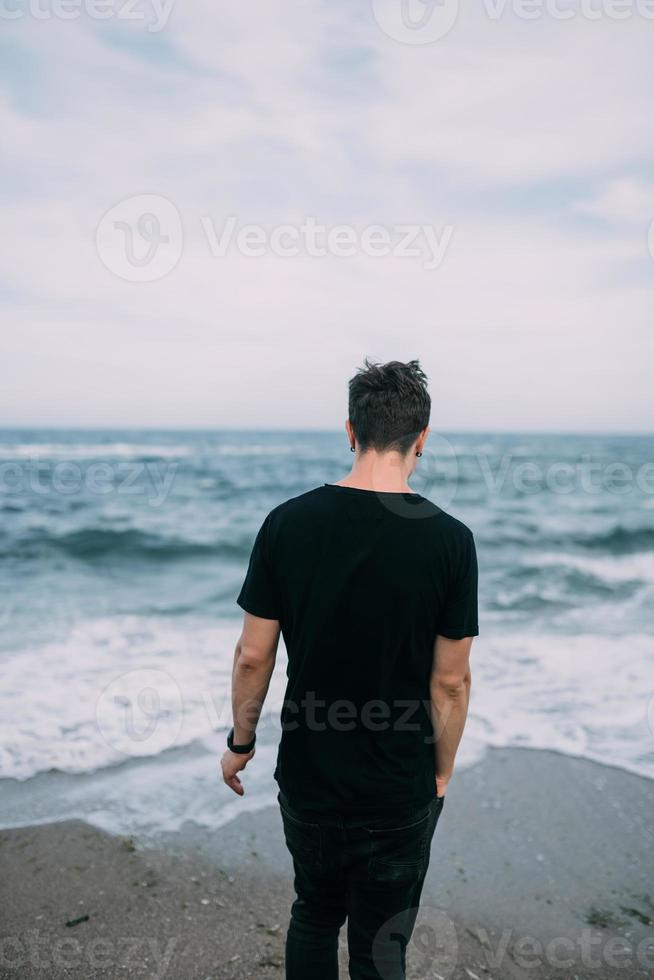 Ein lächelnder Typ in einem schwarzen T-Shirt steht am Sandstrand. foto