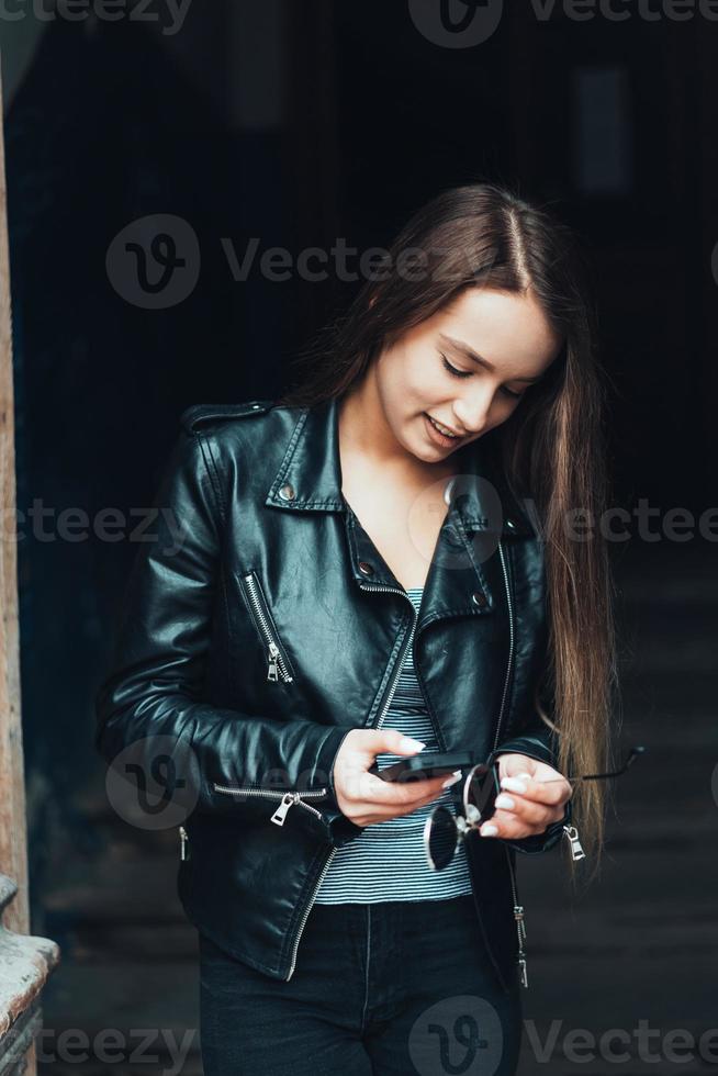 schönes Mädchen in schwarzer Jacke mit Smartphone foto