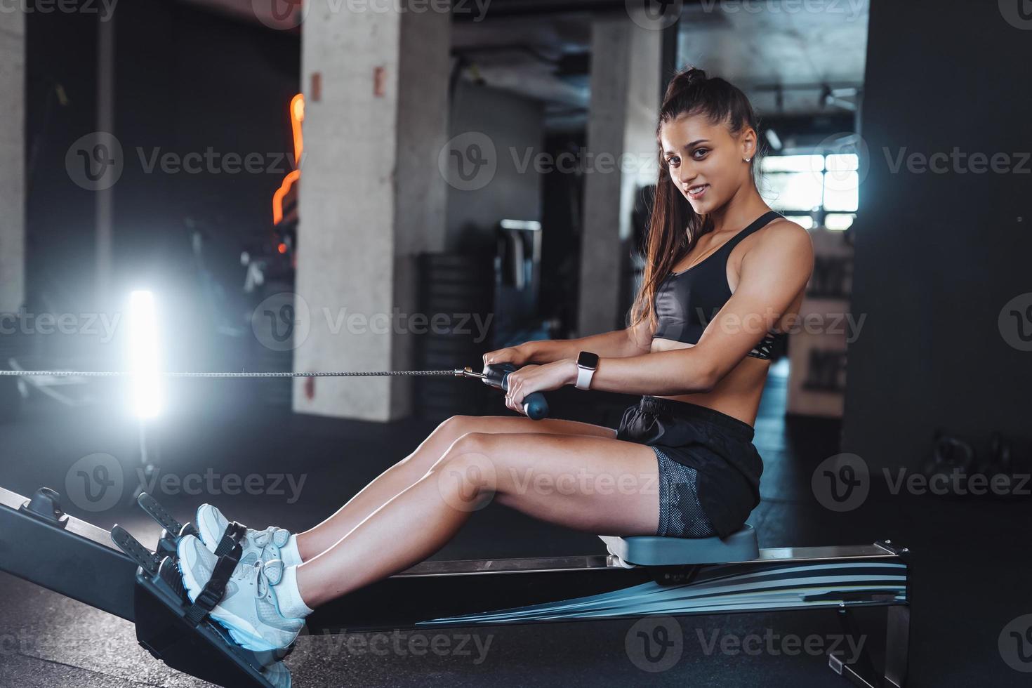 junge Frau trainiert und zieht Gewichte in sitzender Kabelrudermaschine. foto