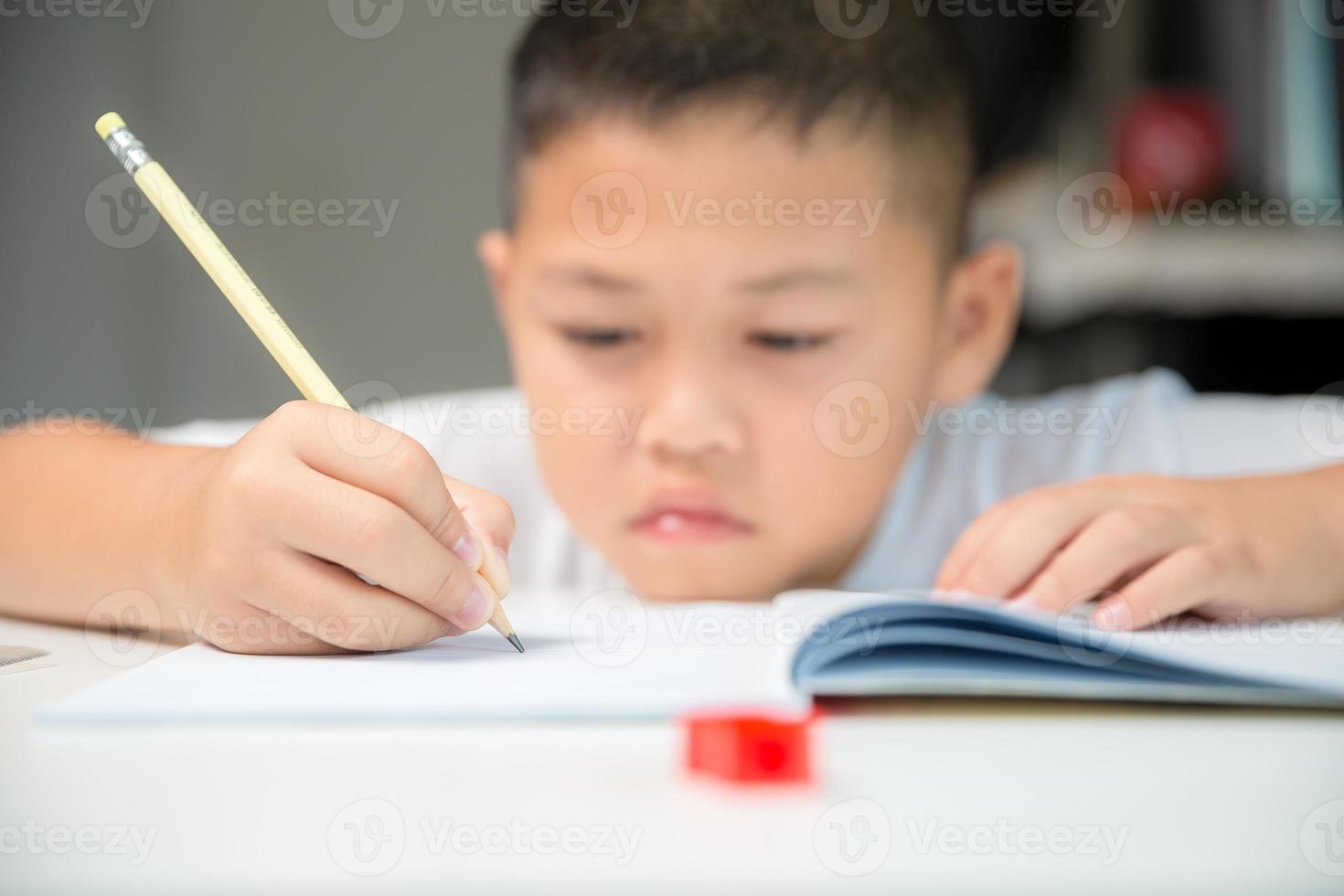 Junge Person sitzt zu Hause drinnen, männlicher Schüler lernt online und macht Hausaufgaben auf dem Schreibtisch, junges Kind liest und schreibt ein Buch auf dem Tisch. konzept der bildung, technologie cyberspace foto