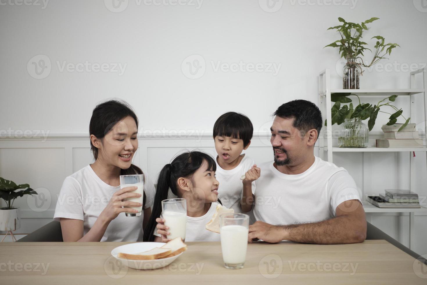 eine gesunde asiatische thailändische familie, kleine kinder und junge eltern trinken morgens frische weiße milch im glas und brotfreude zusammen an einem esstisch, wellness ernährung zuhause frühstücksmahlzeit lebensstil. foto