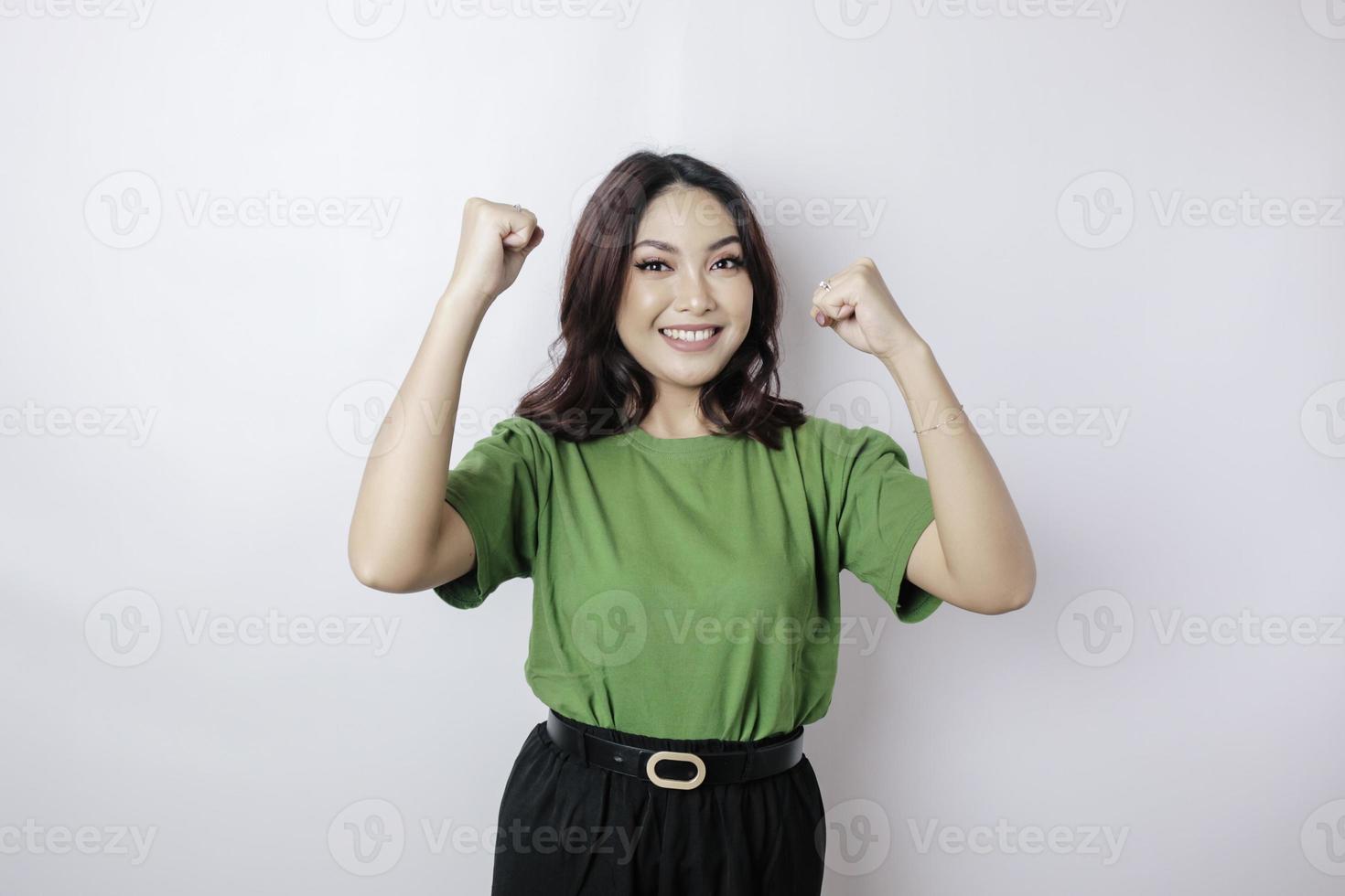 eine junge asiatische Frau mit einem glücklichen erfolgreichen Ausdruck, der das grüne Hemd trägt, das durch weißen Hintergrund getrennt wird foto