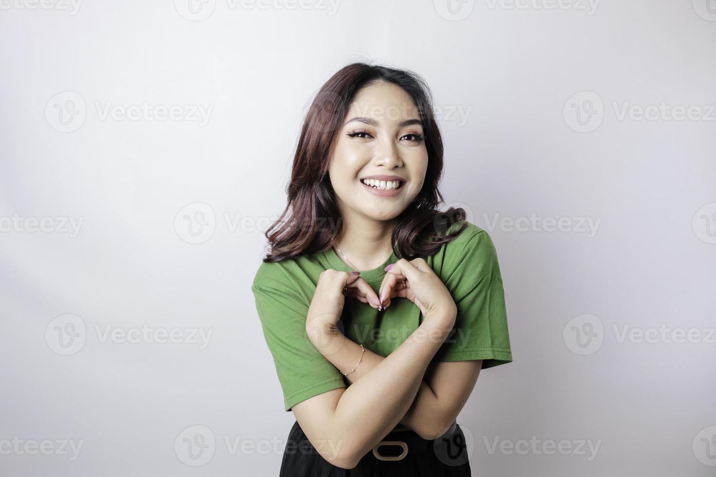 eine attraktive junge asiatische frau, die ein grünes t-shirt trägt, fühlt sich glücklich und eine romantische formherzgeste drückt zärtliche gefühle aus foto