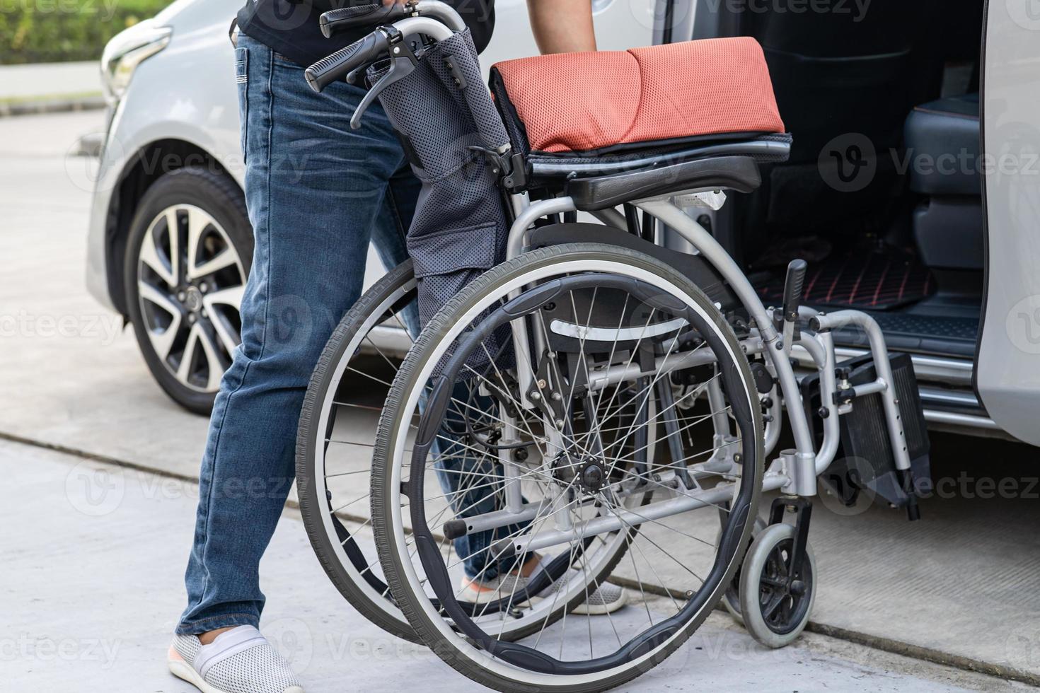 asiatische Frau, die den Rollstuhl in ihr Auto faltet und anhebt. Konzept der Barrierefreiheit. foto