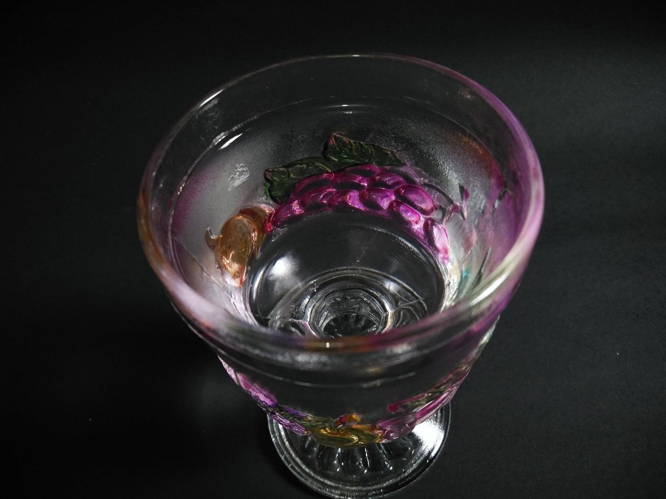 Ein transparentes Glas mit Fruchtmuster, gefüllt mit Mineralwasser auf schwarzem Hintergrund. foto