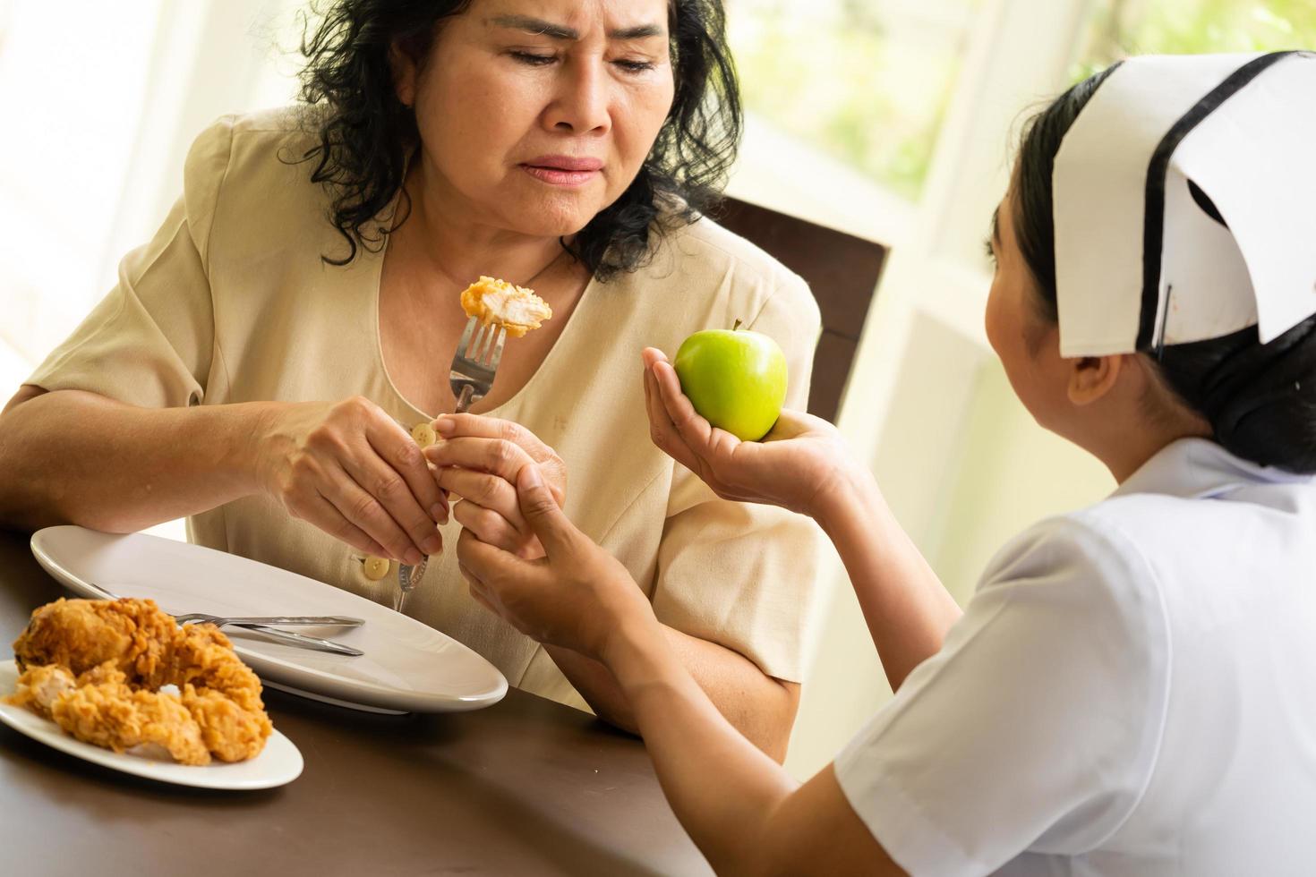 Krankenschwester schlägt erwachsenen weiblichen Patienten vor, Apfel statt gebratenem Hähnchen zu essen. foto