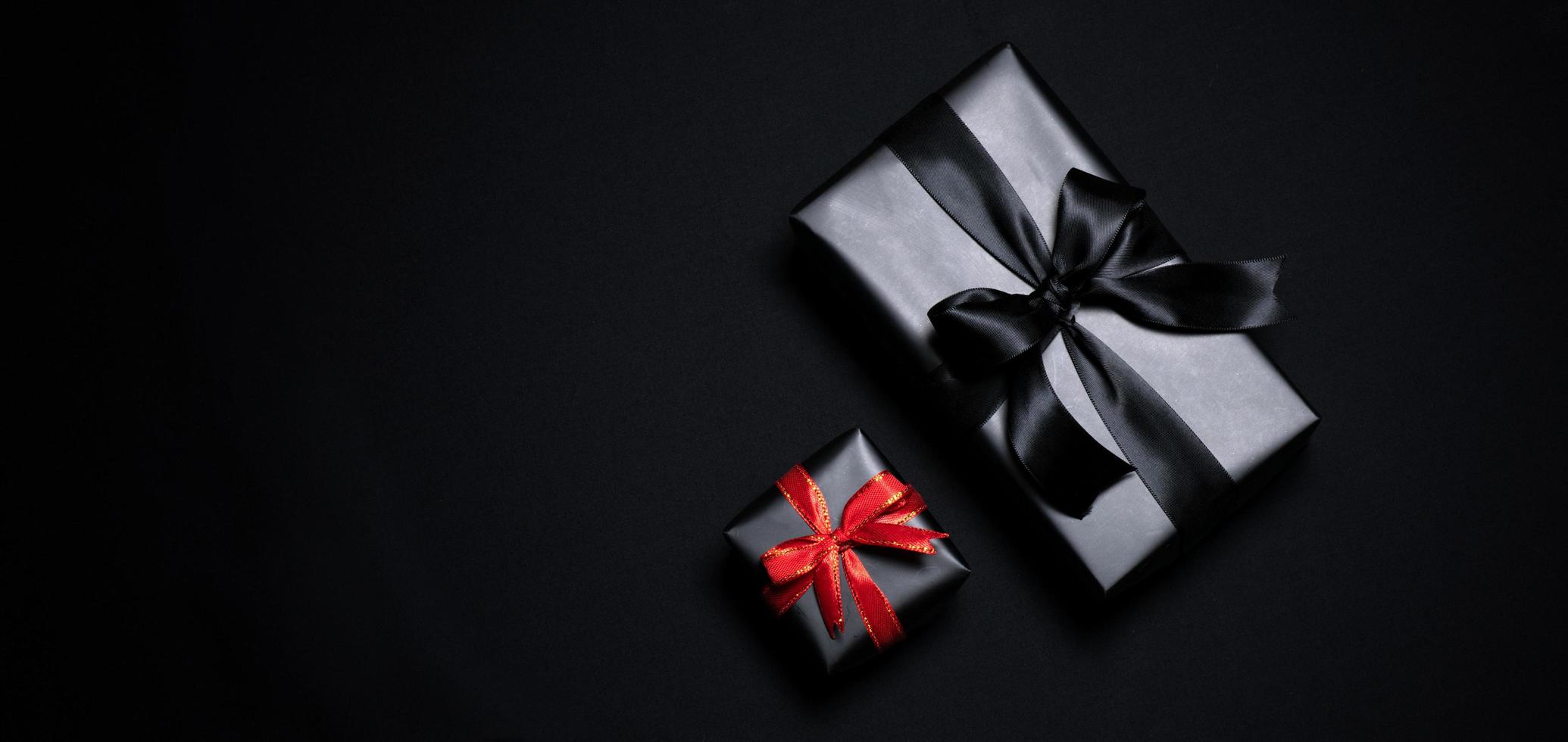 Draufsicht auf schwarze Geschenkbox mit roten und schwarzen Bändern isoliert auf schwarzem Hintergrund. foto