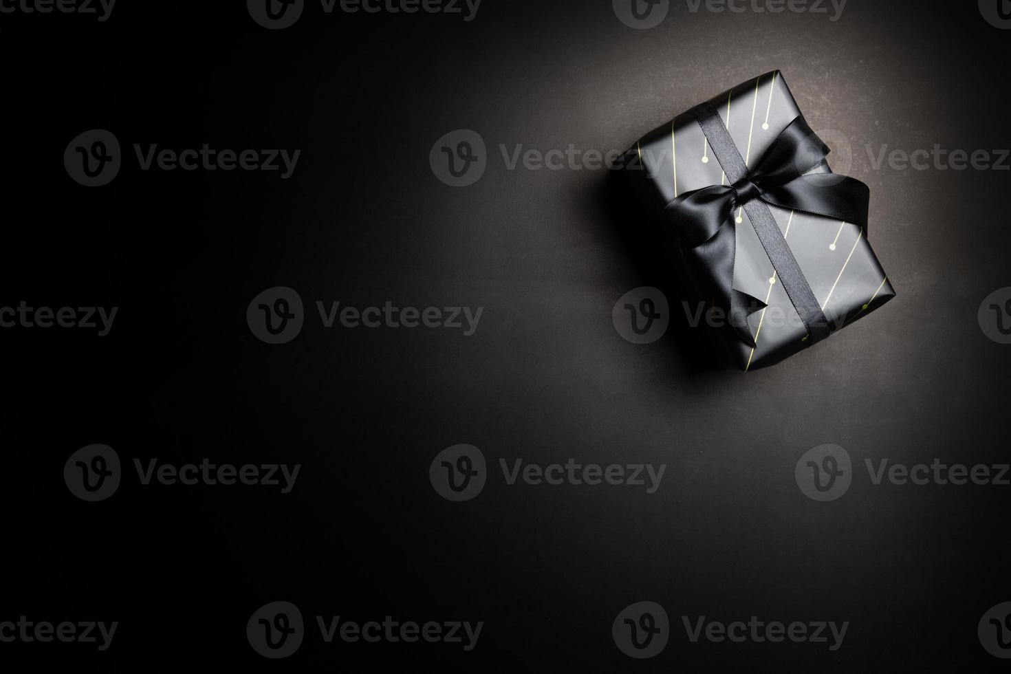 Draufsicht der schwarzen Geschenkbox mit schwarzen Bändern isoliert auf schwarzem Hintergrund. foto