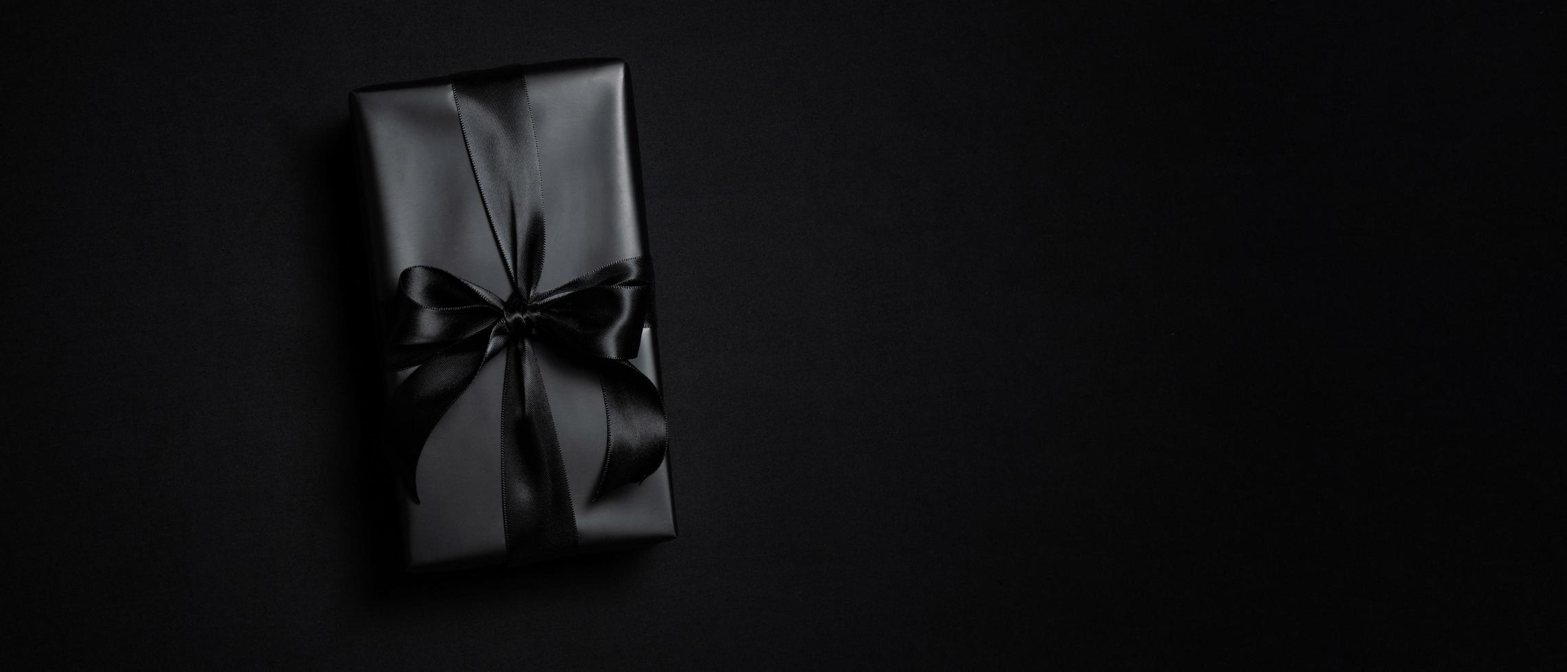 Draufsicht der schwarzen Geschenkbox mit schwarzen Bändern isoliert auf schwarzem Hintergrund. foto