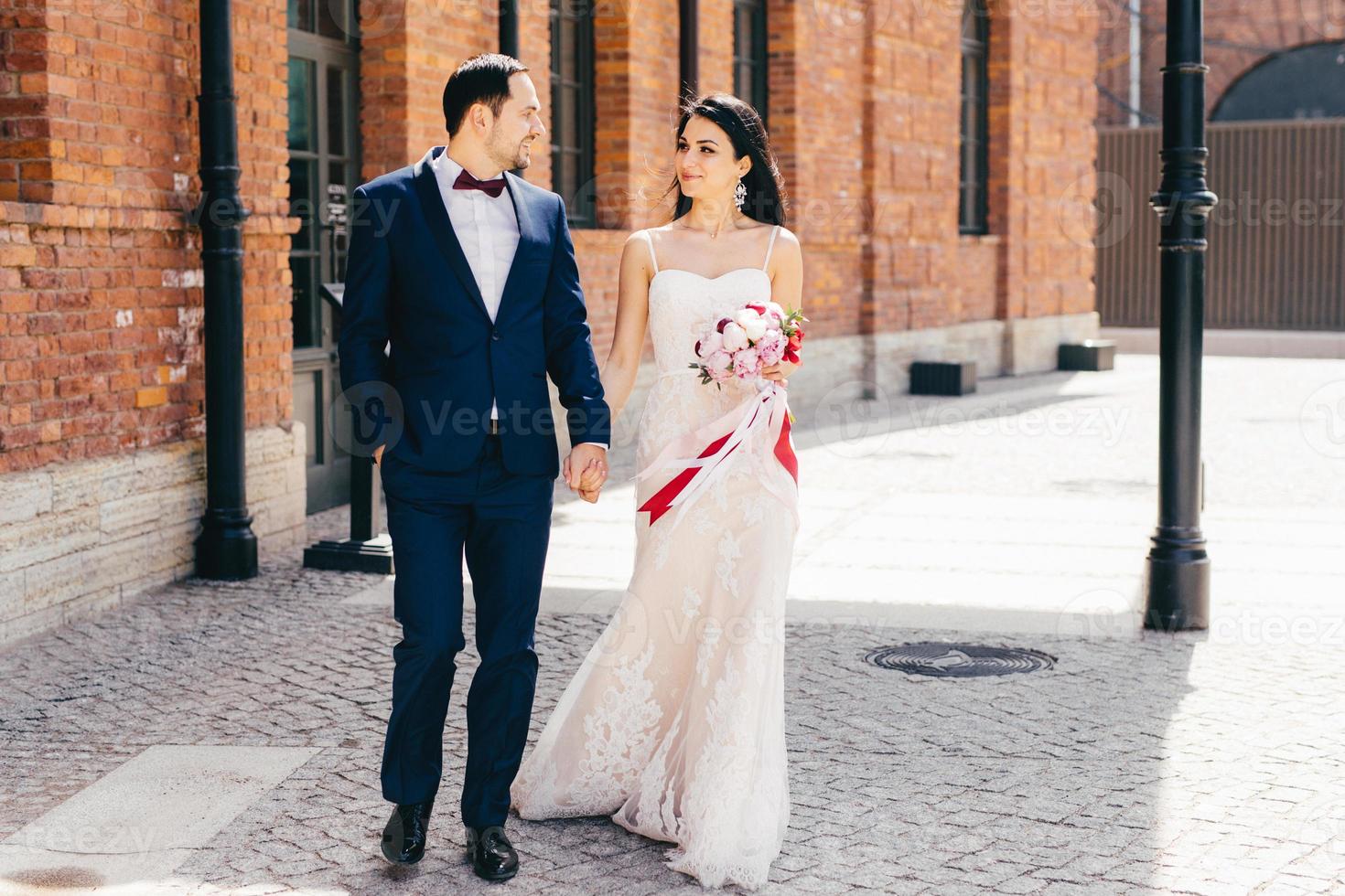 Menschen, Beziehung und Liebeskonzept. brünette attraktive braut in schönem weißem kleid, hält blumenstrauß, hält ihre geliebte hand, hat angenehme gespräche, genießt zusammengehörigkeit und ruhe foto