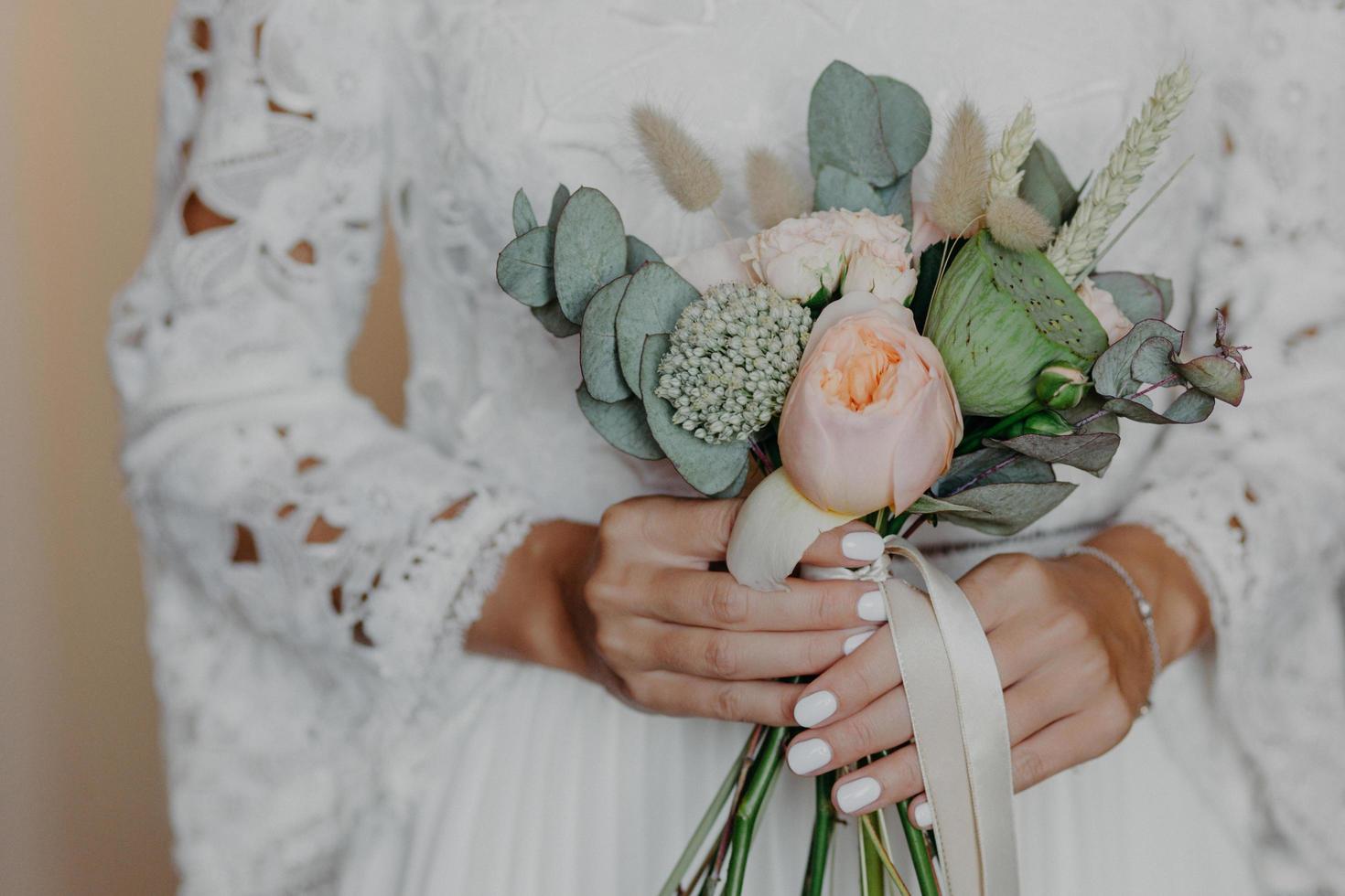 nicht erkennbare braut mit zarter maniküre, hält schönen blumenstrauß, trägt weißes hochzeitskleid. besonderer anlass, zeremoniekonzept foto