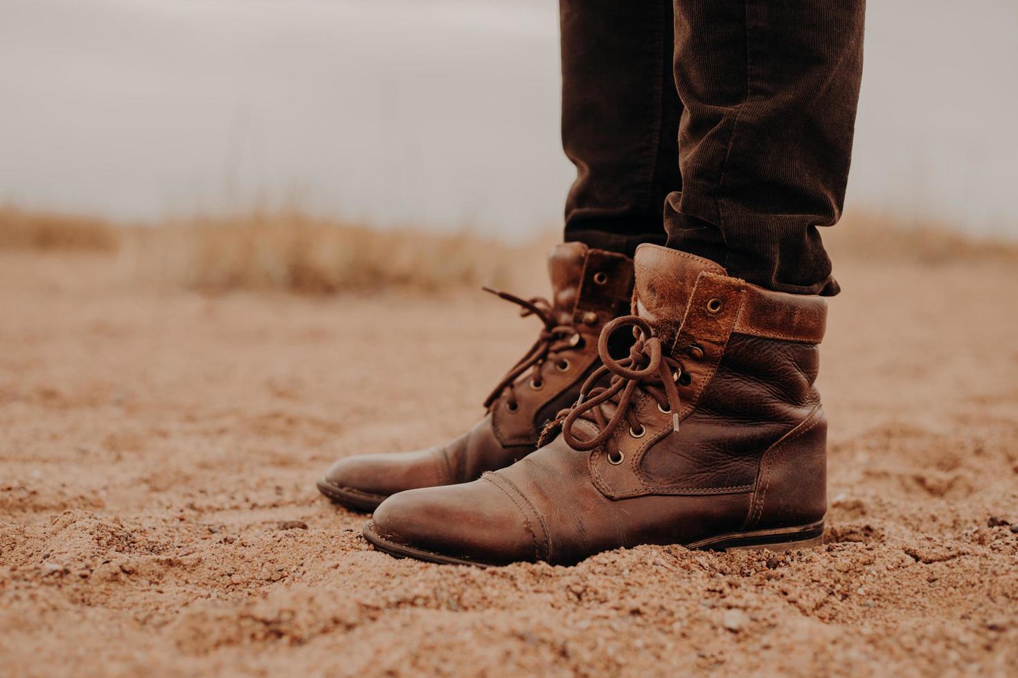 Seitlicher Schuss eines Mannes in zotteligen braunen Schuhen auf einer Liegefläche. Paar Stiefel auf Sand. Männchen hat einen Spaziergang im Freien in alten Schuhen. foto