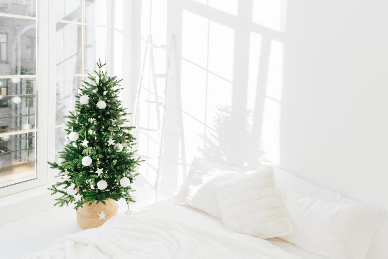 geschmückter festlicher weihnachtsbaum im weißen klassischen schlafzimmerinnenraum mit weichem bett. Innenraum des Winterhauses. gemütliche Jahreszeit. Neujahr Feierlichkeiten foto