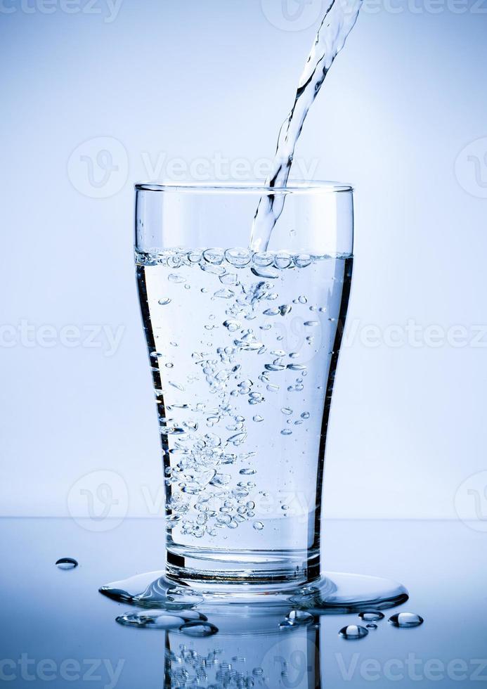 Gießen von frischem, reinem Wasser aus der Flasche in ein Glas auf dem Tisch mit Wassertropfen, Gesundheits- und Schönheitshydratationskonzept foto