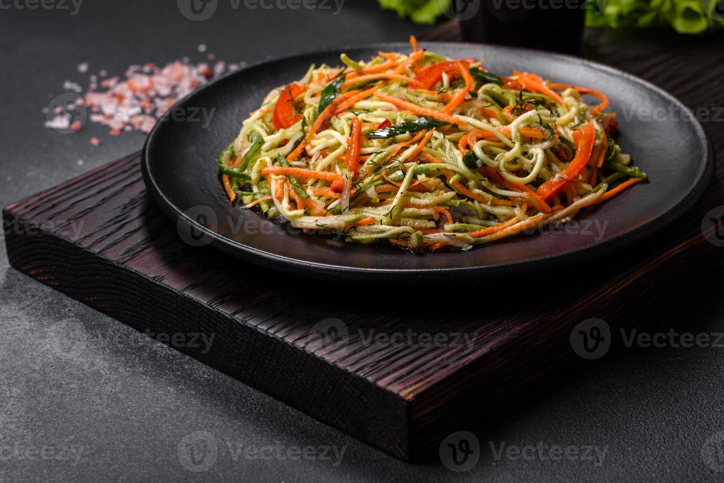 Frischer Salat aus geschnittenen dünnen Karotten- und Zucchinistreifen auf Betongrund foto