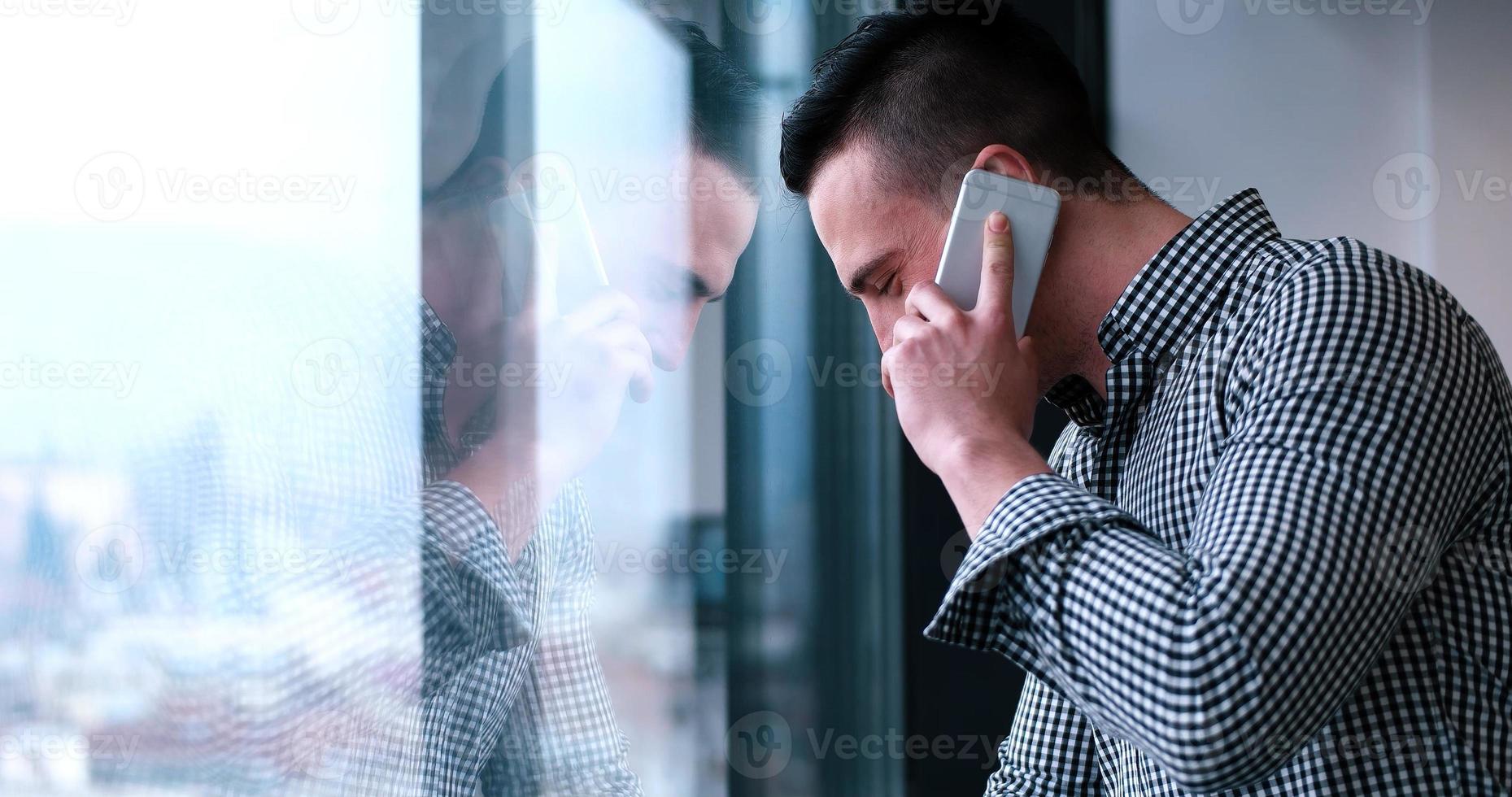 Geschäftsmann, der am Handy spricht und aus dem Bürofenster schaut foto