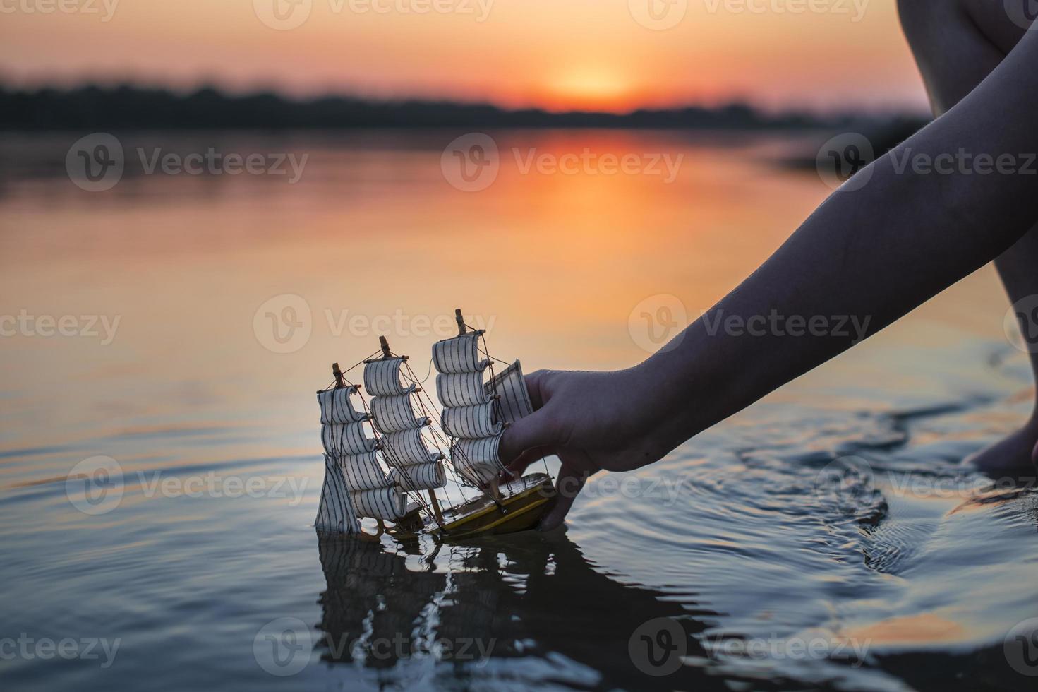 Ein Junge startet bei Sonnenuntergang ein dekoratives Spielzeugschiff. Kindererholung im Freien im Sommer. foto