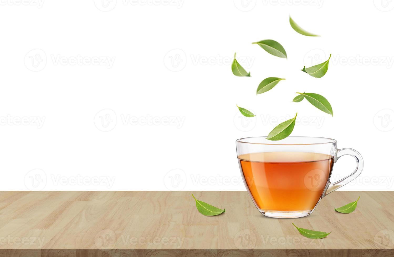 Heiße Tasse Tee auf dem Holztisch mit fliegenden grünen Teeblättern in der Luft, gesunde Produkte aus biologischem, natürlichem Zutatenkonzept, leerer Raum in Studioaufnahme isoliert auf weißem Hintergrund foto