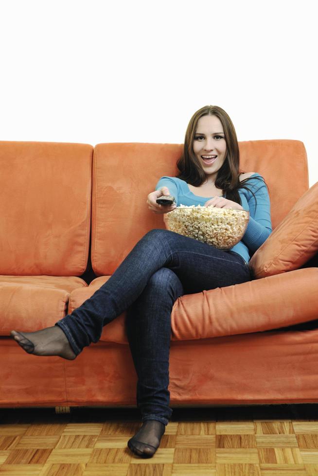 Junge Frau isst Popcorn auf orangefarbenem Sofa foto