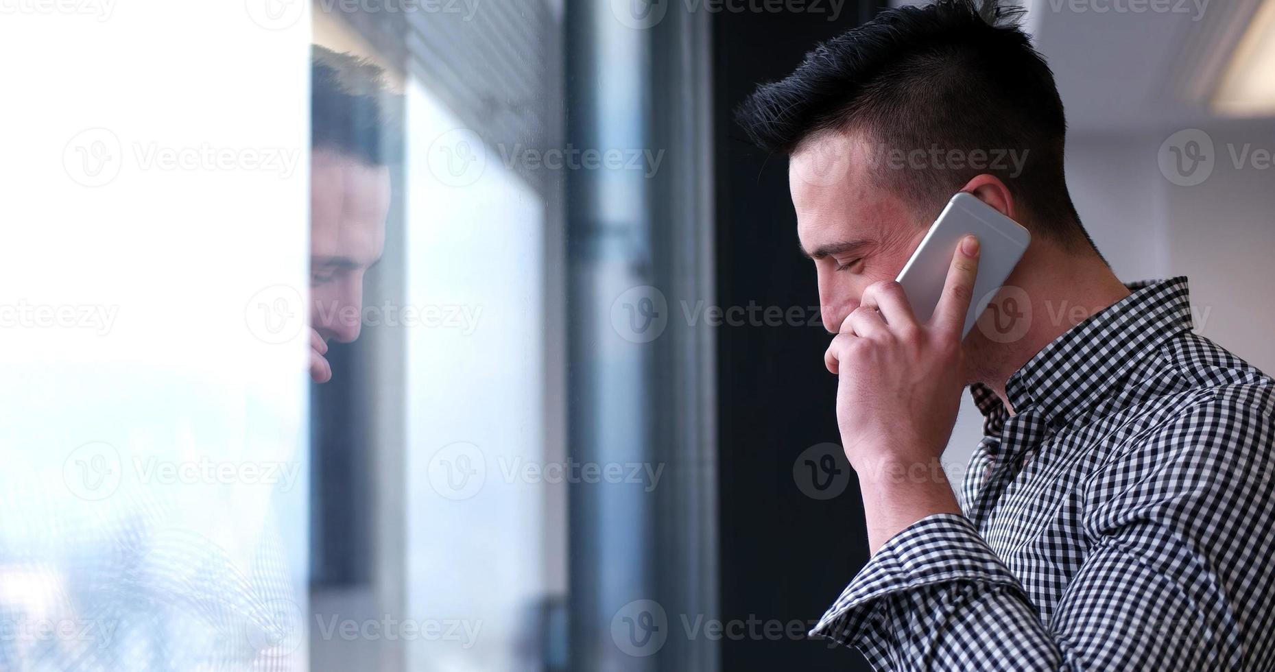 Geschäftsmann, der am Handy spricht und aus dem Bürofenster schaut foto