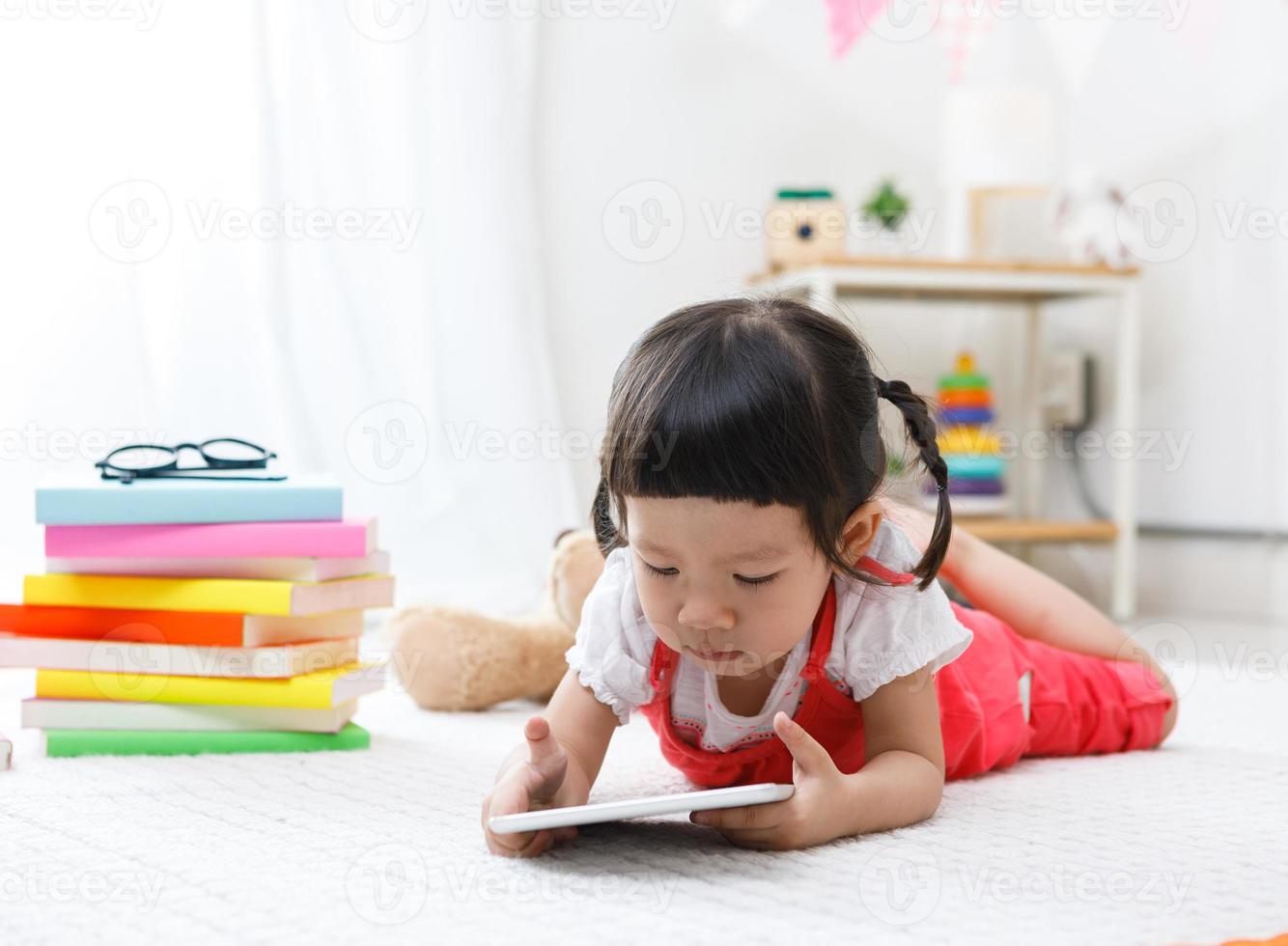 Vorschulmädchen, das Tablette schiebt. süßes kind, das mit teddybär liest. kleines Mädchen, das sich zu Hause, im Kindergarten oder im Kindergarten amüsiert foto