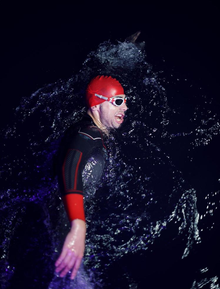 echter triathlonsportler, der in dunkler nacht schwimmt foto