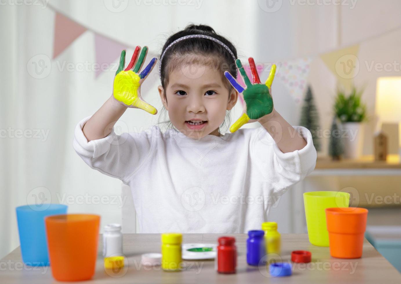 kindliche kreativität, kleine asiatische mädchenhände, die im klassenzimmer zu hause in bunten farben bemalt sind, pädagogisches konzept für die schule foto