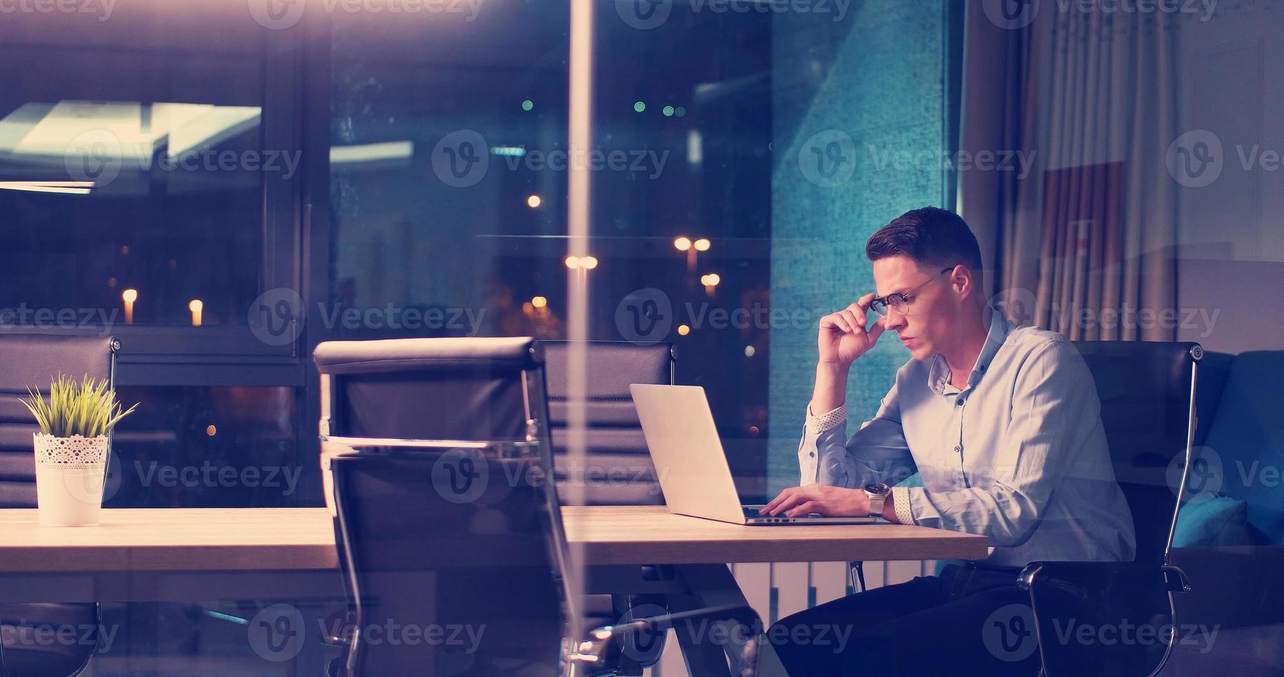 Mann, der im dunklen Büro am Laptop arbeitet foto