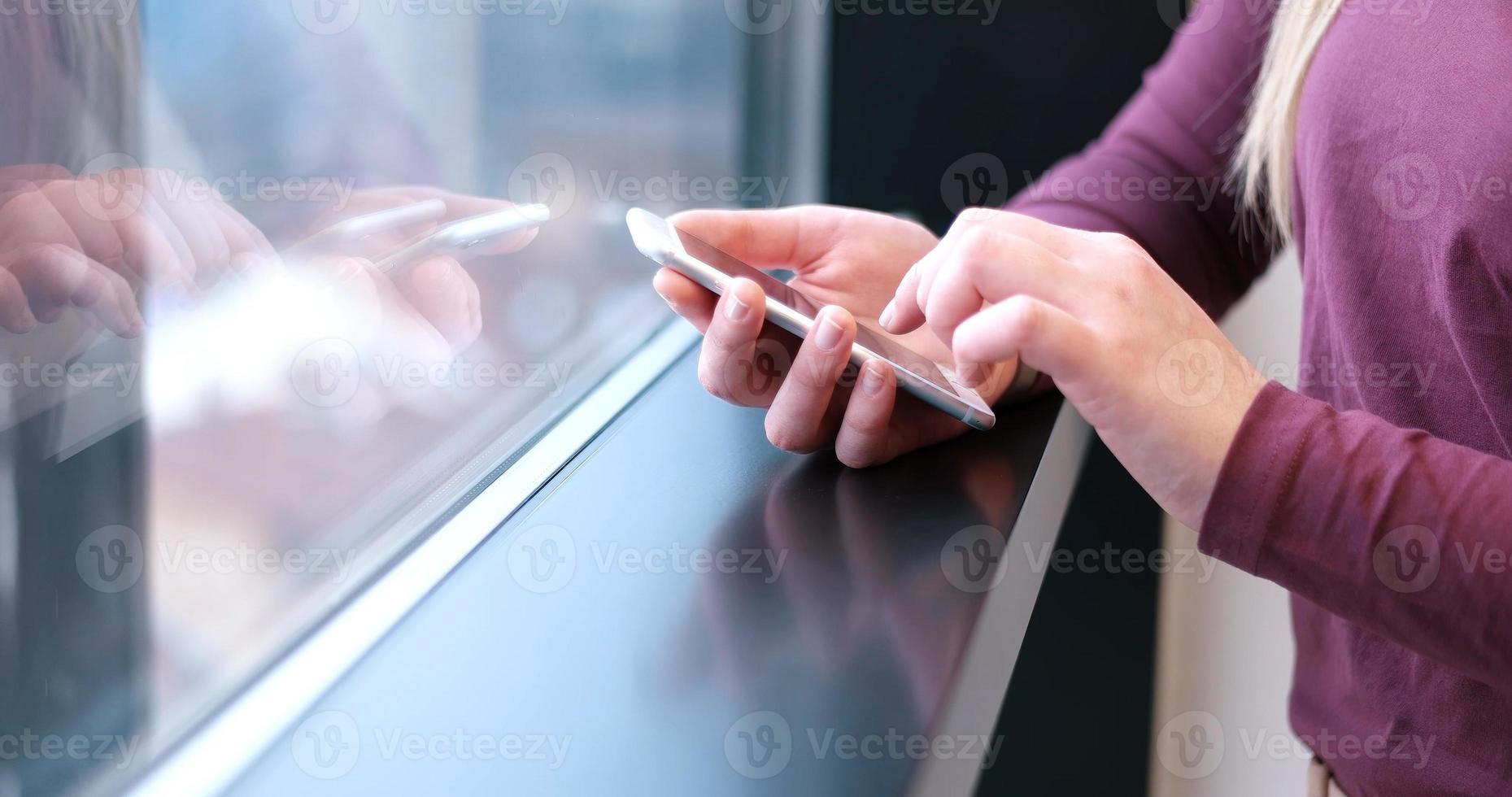 elegante Frau mit Handy durch Fenster im Bürogebäude foto