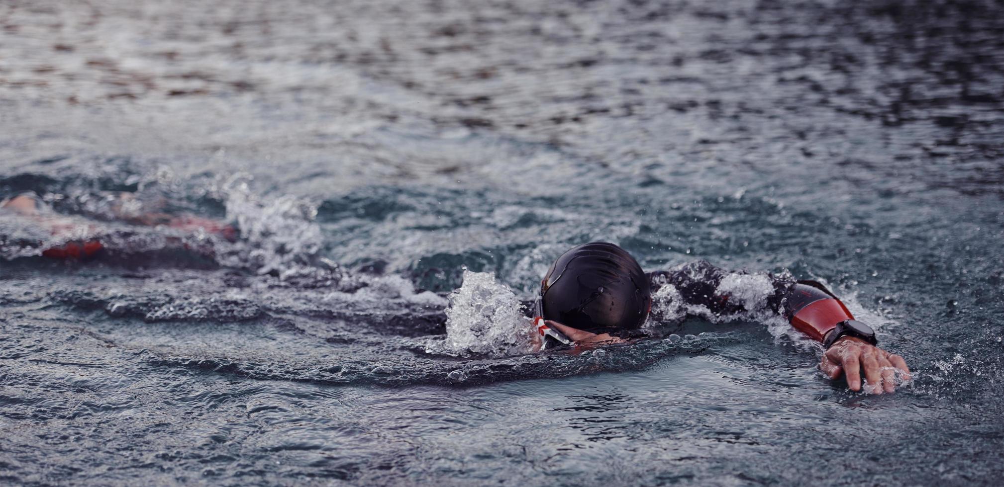 Triathlon-Athlet, der bei Sonnenaufgang auf dem See schwimmt und einen Neoprenanzug trägt foto