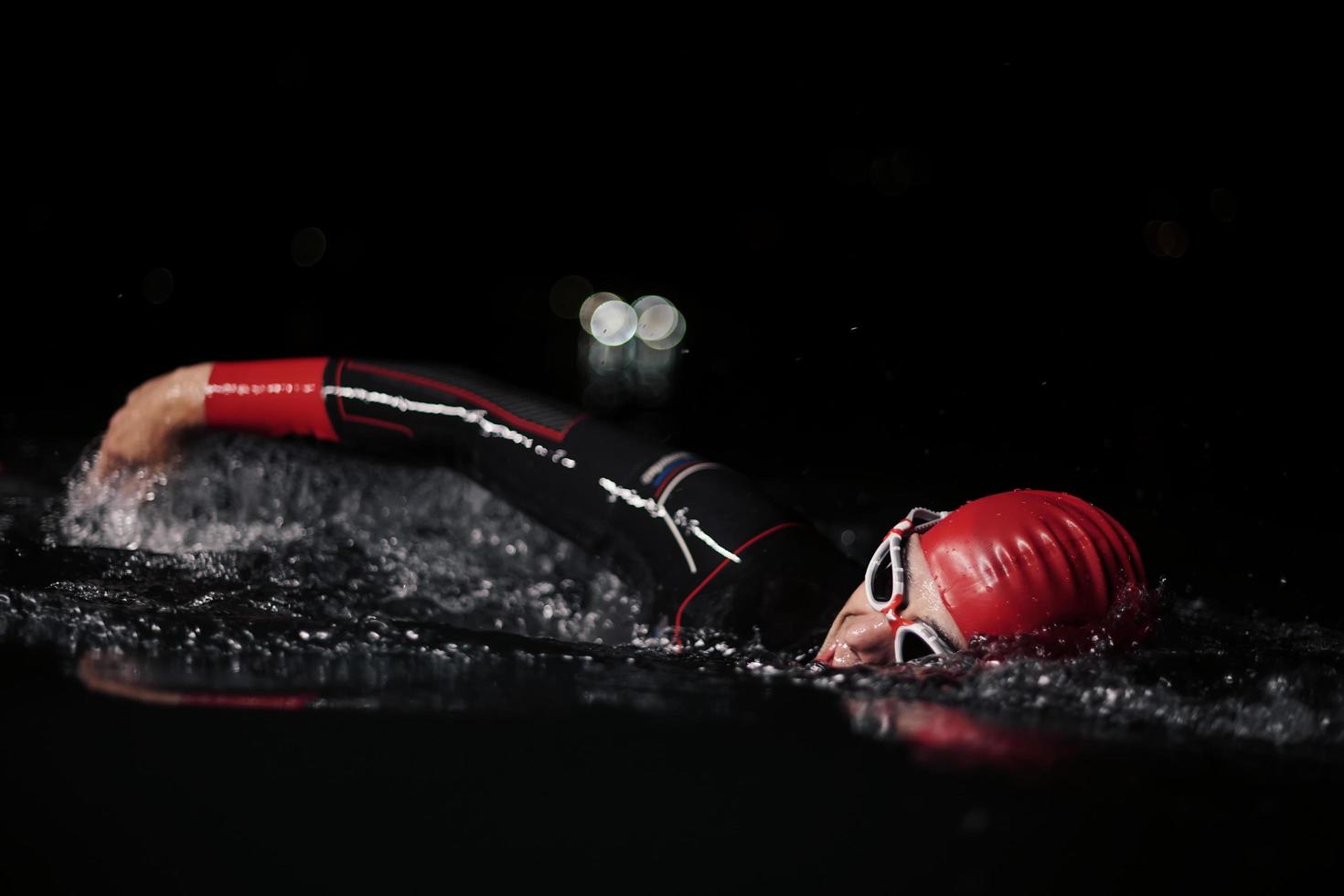 Triathlon-Athlet schwimmt in dunkler Nacht und trägt einen Neoprenanzug foto