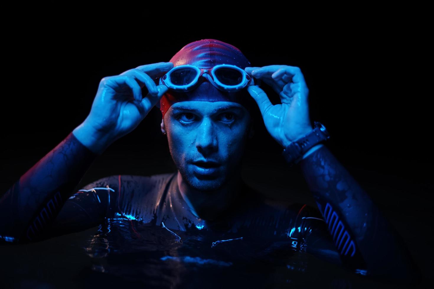 Authentischer Triathlet-Schwimmer, der während des harten Trainings im nächtlichen Neon-Gel-Licht eine Pause macht foto