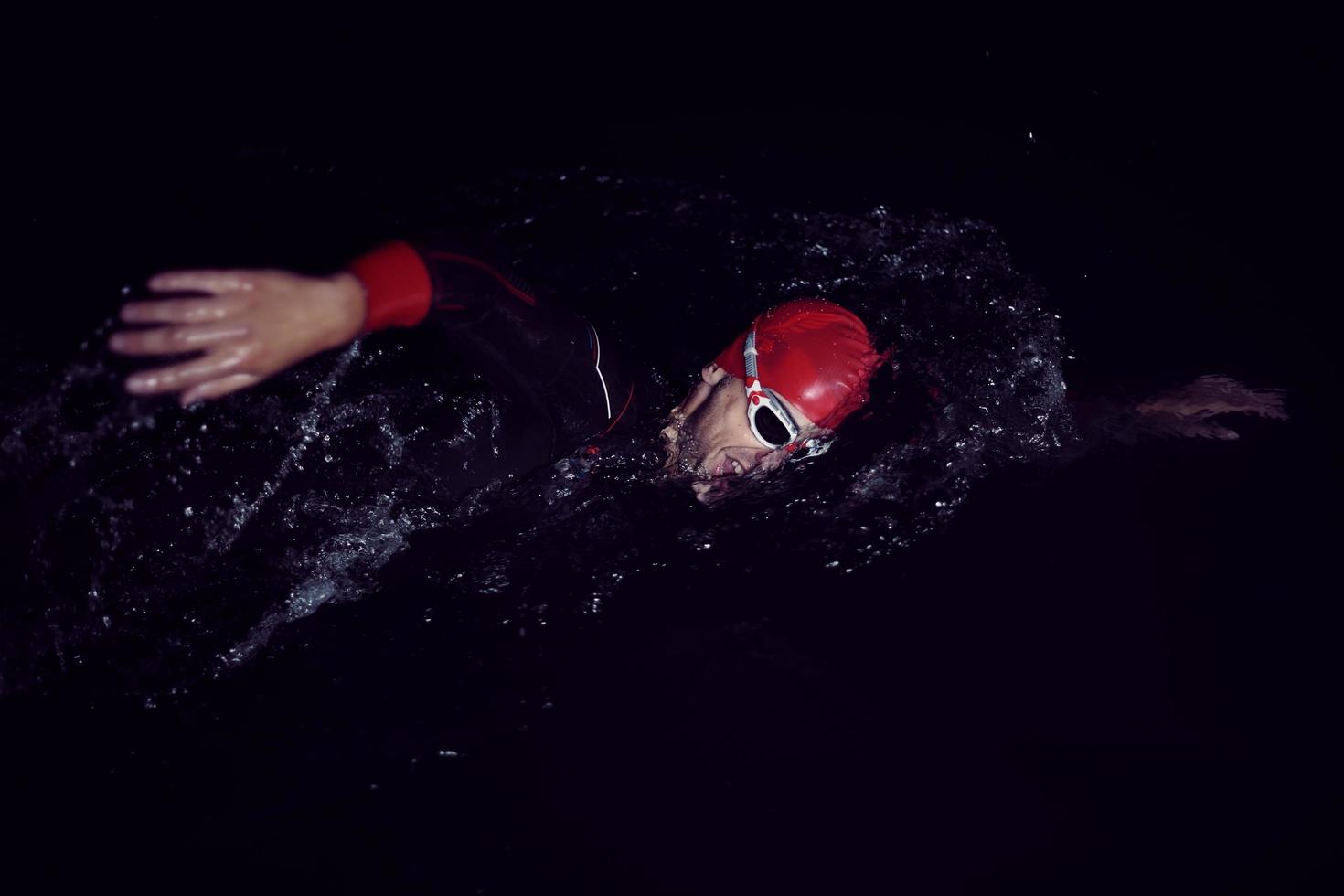 Triathlon-Athlet schwimmt in dunkler Nacht und trägt einen Neoprenanzug foto
