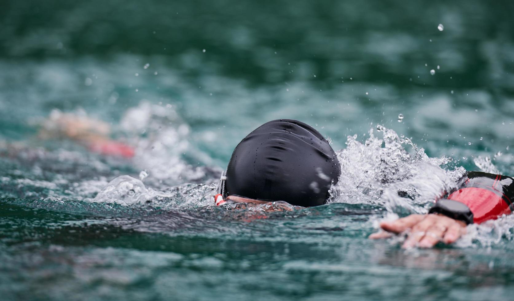 Triathlon-Athlet, der auf dem See schwimmt und einen Neoprenanzug trägt foto