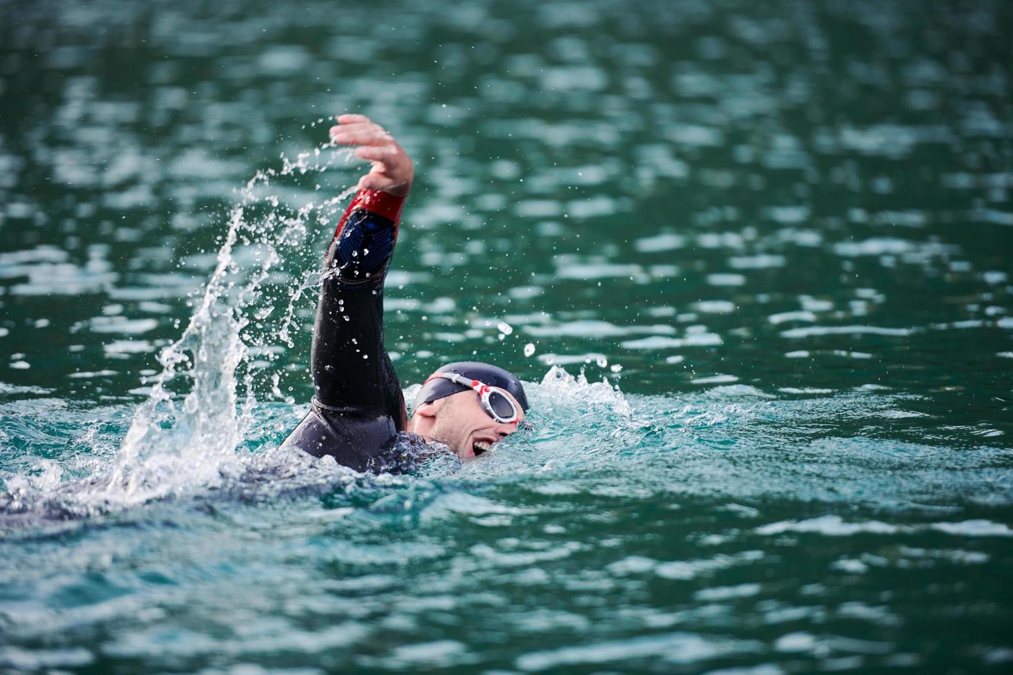 Triathlon-Athlet, der bei Sonnenaufgang auf dem See schwimmt und einen Neoprenanzug trägt foto