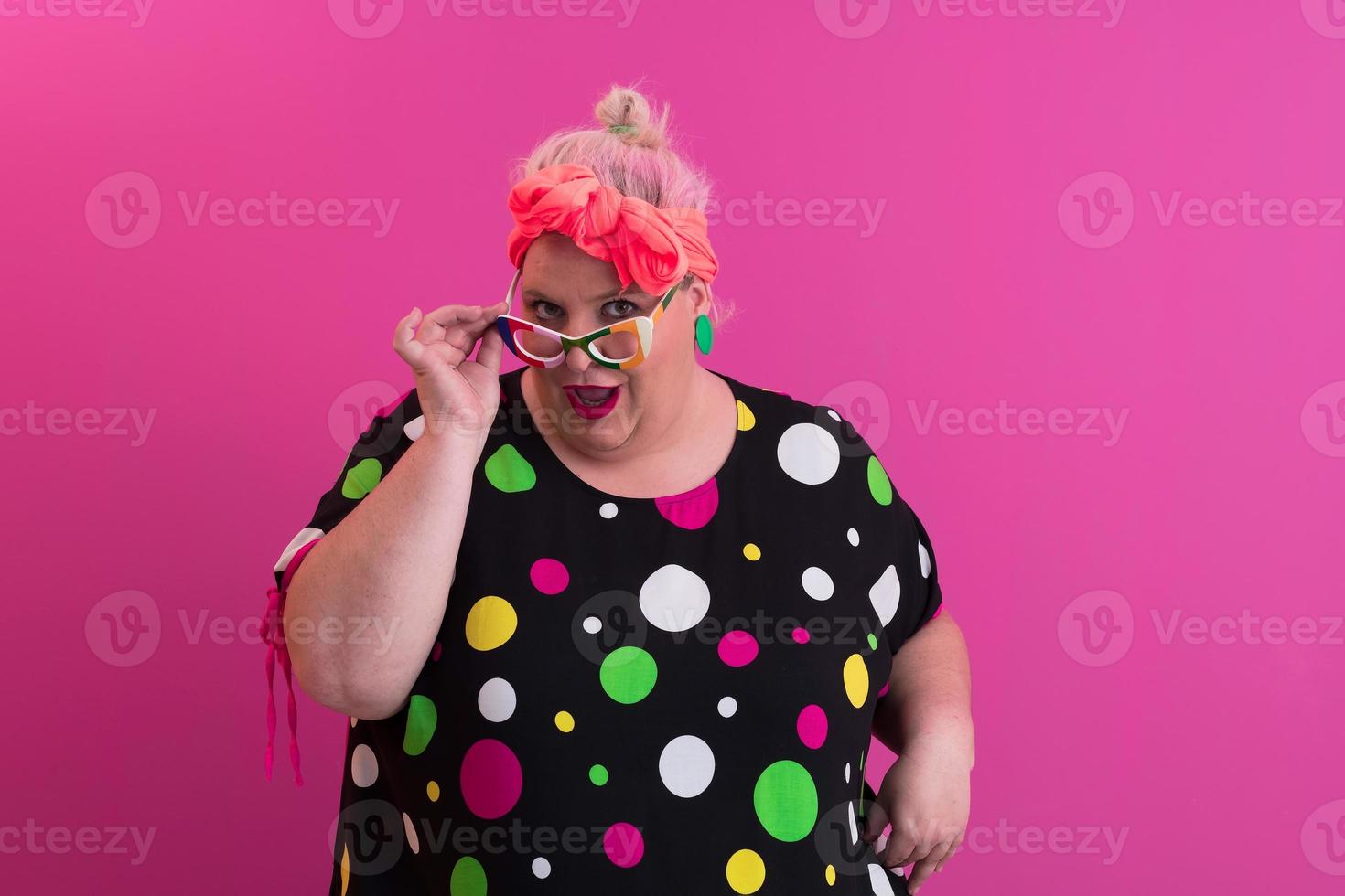 glückliche Frau in Übergröße, die eine Brille trägt und in die Kamera lächelt, die über rosa Hintergrund steht. fröhliche tausendjährige frau in brillen posiert im studio. foto